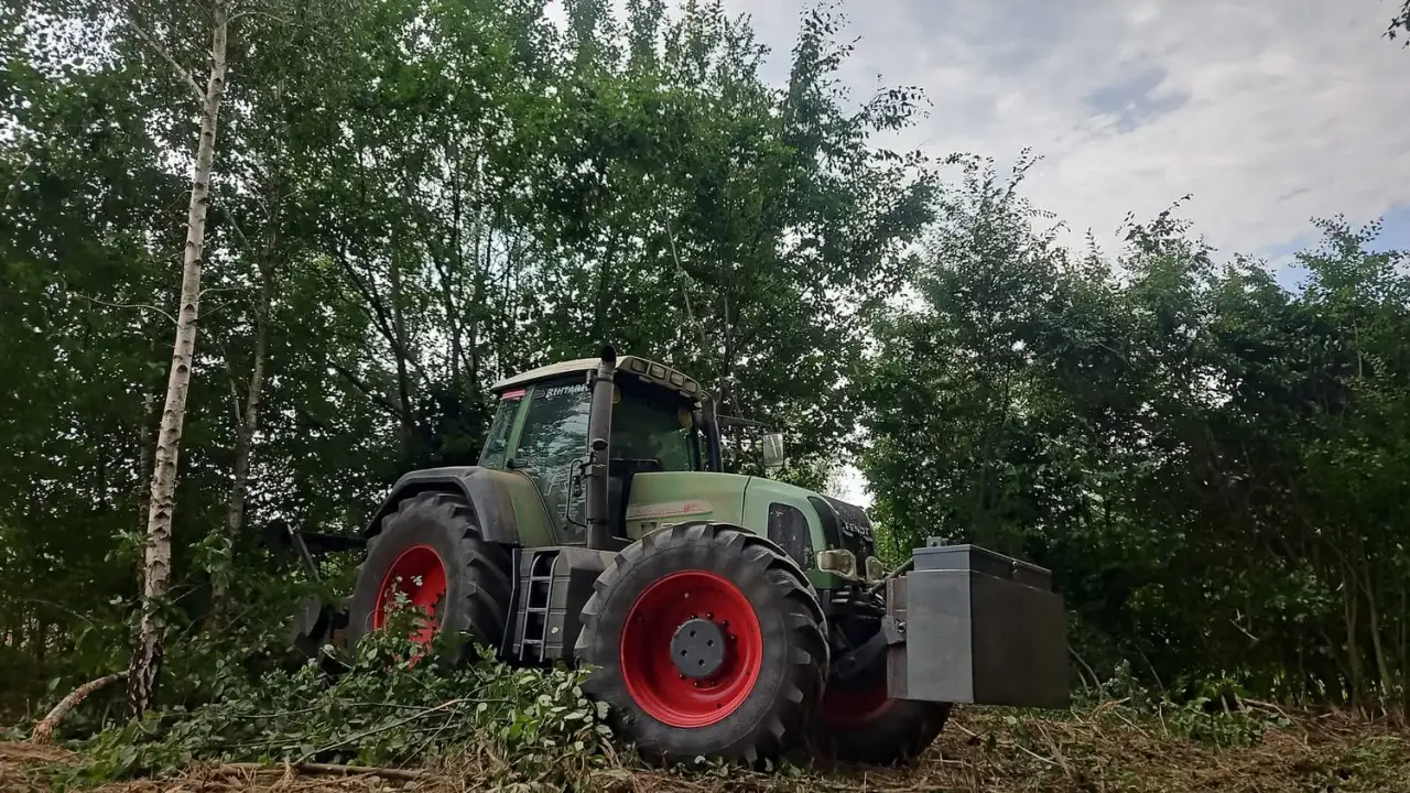 Traktor s malčerom u zaraslom raslinju i mladom drveću